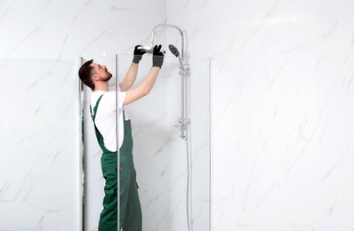 Photo of Professional handyman working in shower booth indoors, space for text