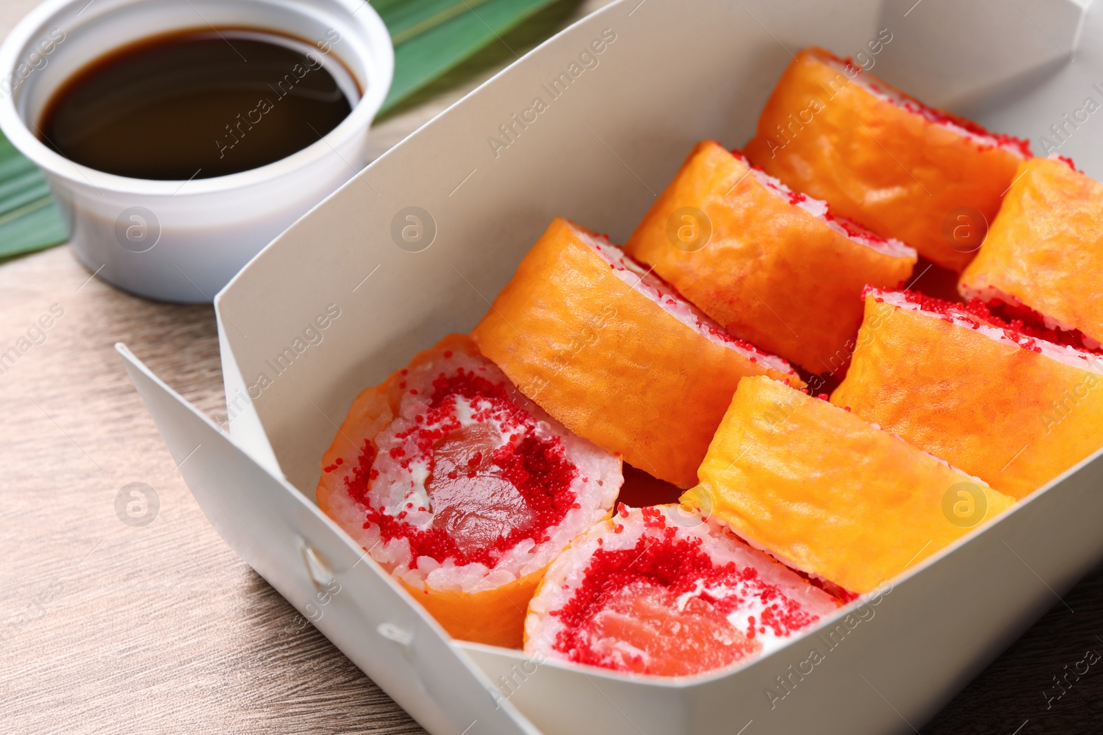 Photo of Food delivery. Paper box with delicious sushi rolls and soy sauce on wooden table, closeup