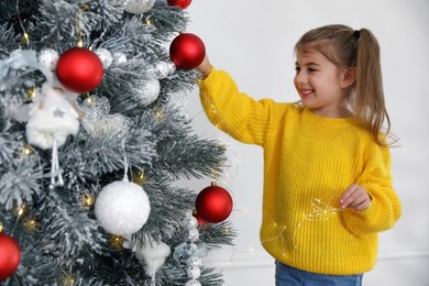 Photo of Cute little girl decorating Christmas tree at home