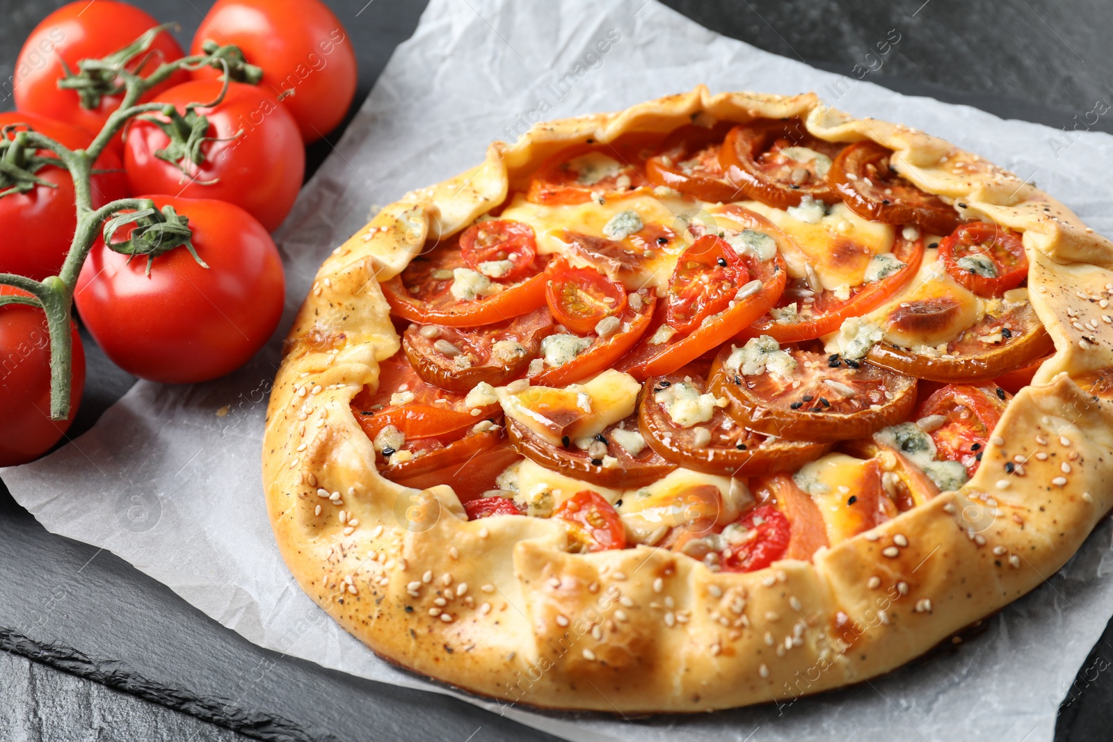 Photo of Tasty galette with tomato and cheese (Caprese galette) on dark table, closeup