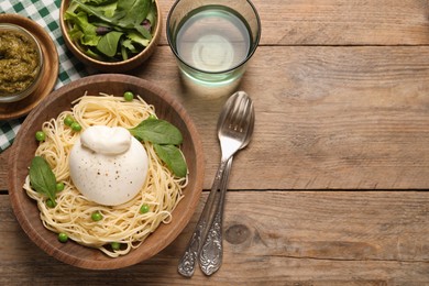 Photo of Bowl of delicious pasta with burrata, peas and spinach served on wooden table, flat lay. Space for text