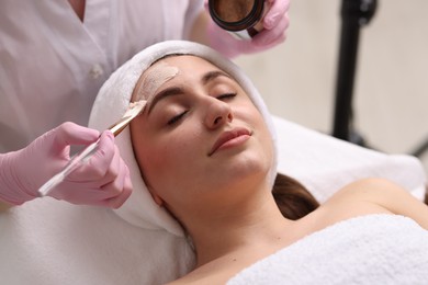 Photo of Cosmetologist applying mask on woman's face in clinic, closeup