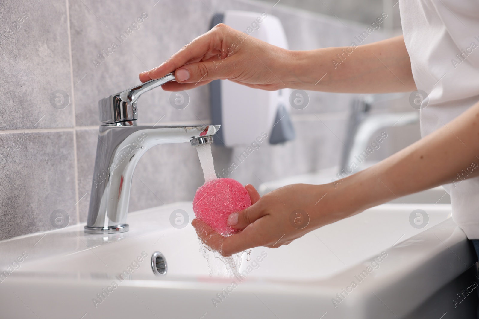 Photo of Young woman washing face sponge in bathroom, closeup