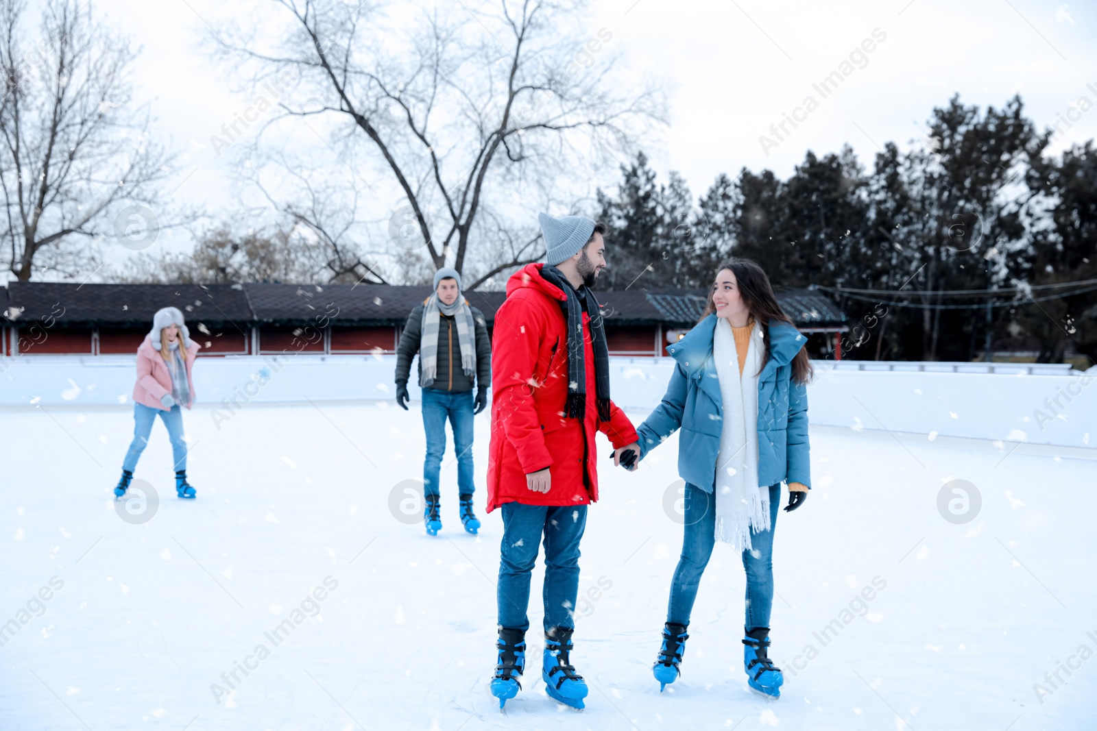 Image of Happy couple with friends skating along ice rink outdoors