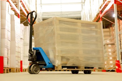 Modern manual forklift with wrapped wooden pallets in warehouse