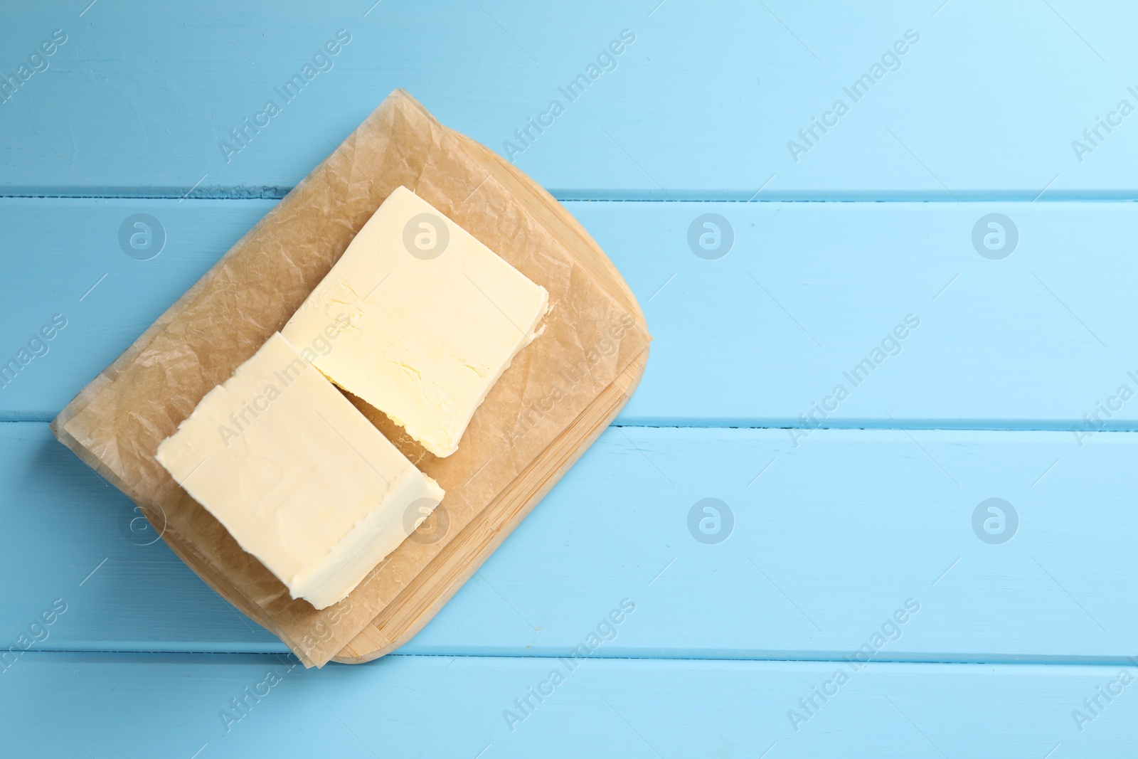 Photo of Block of tasty butter on light blue wooden table, top view. Space for text