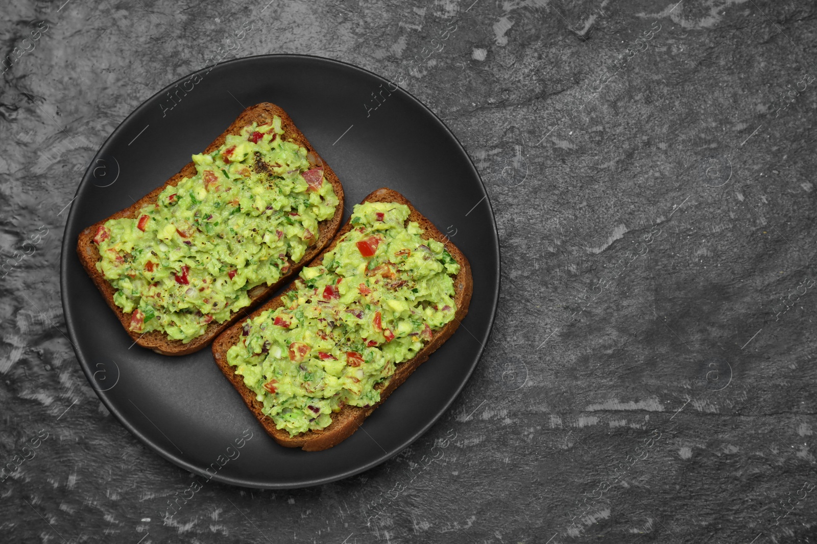 Photo of Slices of bread with tasty guacamole on black textured table, top view. Space for text