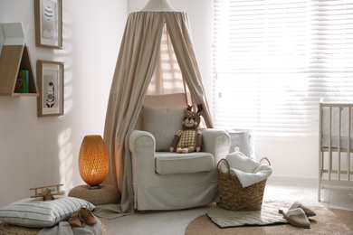 Photo of Stylish baby room interior with crib and comfortable armchair