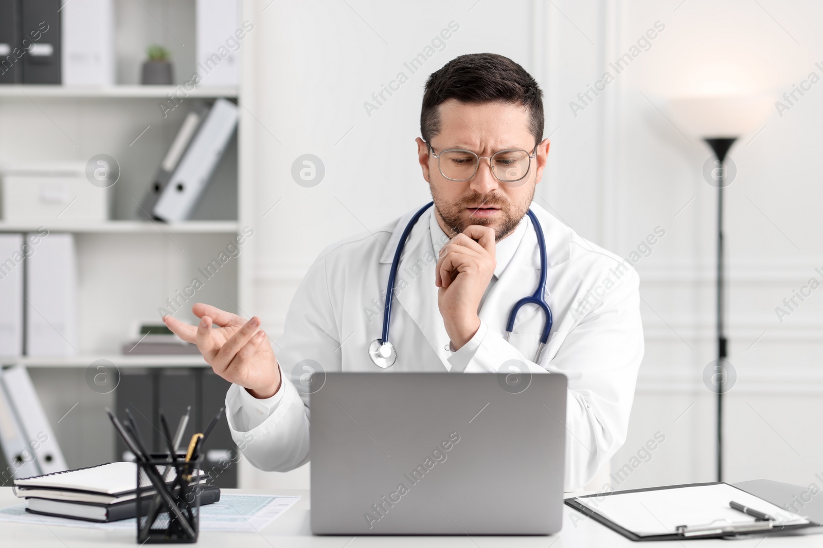 Photo of Doctor having online consultation via laptop at table in clinic