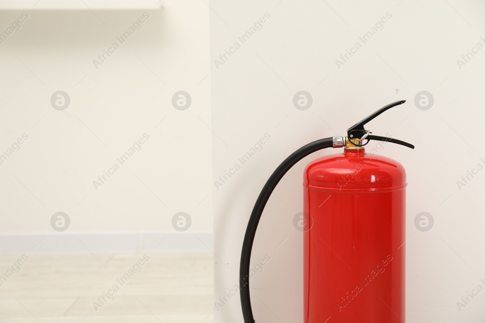 Photo of Fire extinguisher near light wall indoors, space for text