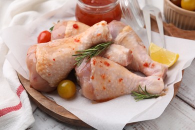 Photo of Marinade, raw chicken drumsticks, rosemary and tomatoes on white wooden table, closeup