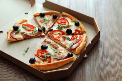 Cardboard box with tasty pizza on wooden background