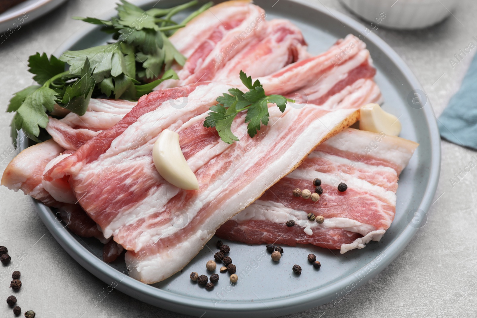Photo of Slices of tasty pork fatback with spices on grey table, closeup