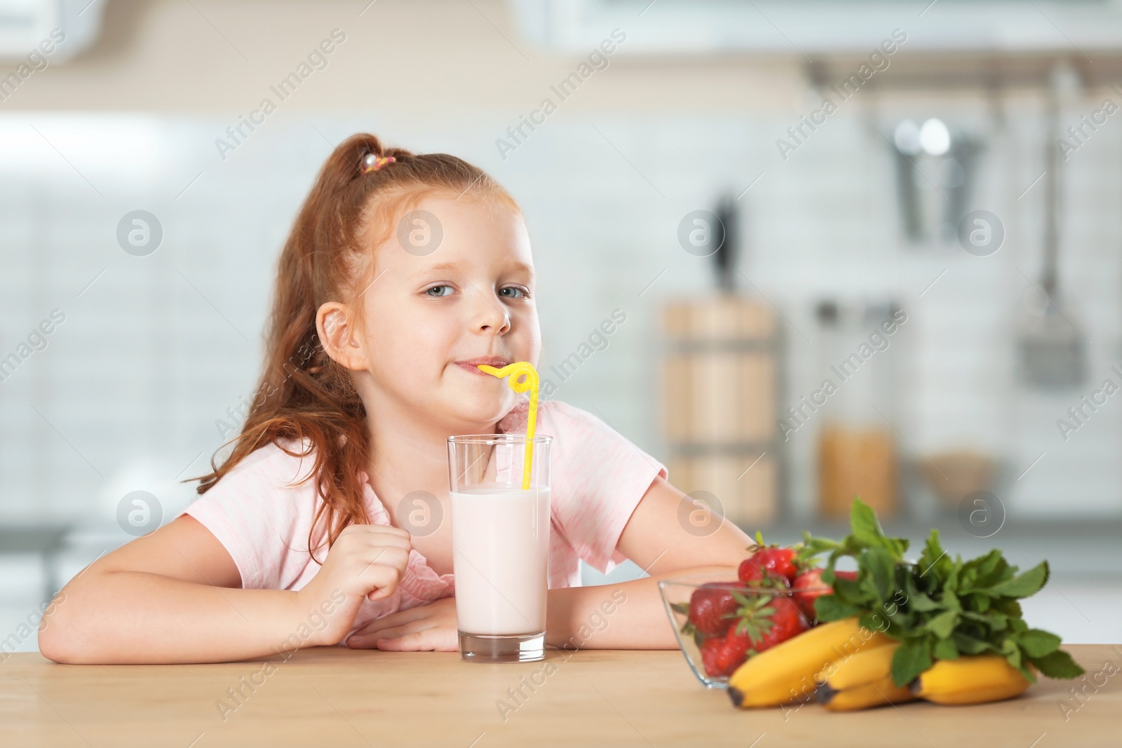 Photo of Little girl with glass of delicious milk shake in kitchen