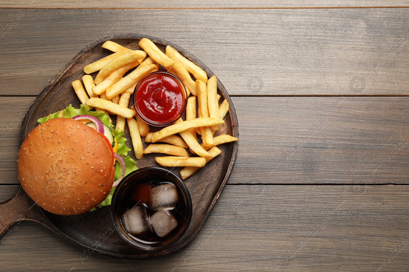 Photo of French fries, tasty burger, sauce and drink on wooden table, top view. Space for text