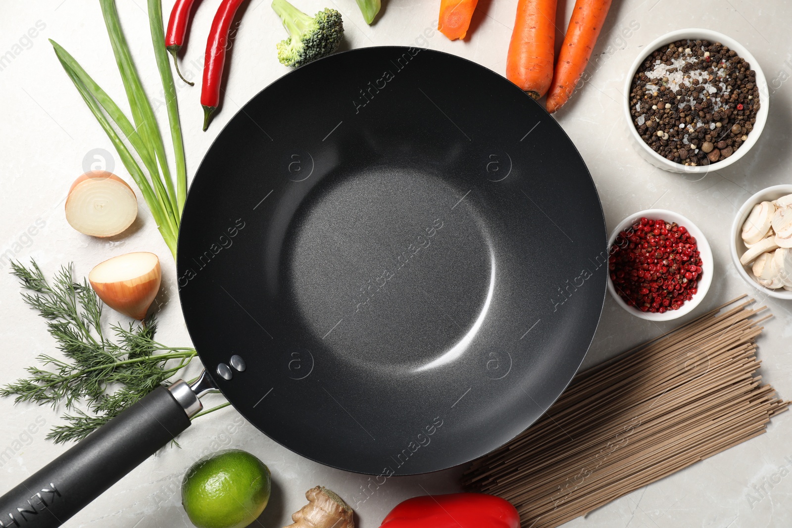 Photo of Empty iron wok surrounded by raw ingredients on light table, flat lay