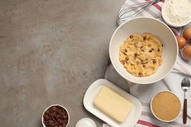 Photo of Fresh dough and different ingredients for cooking chocolate chip cookies on grey table, flat lay. Space for text