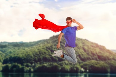 Image of Superhero, motivation and power. Man in cape and mask over lake in mountains