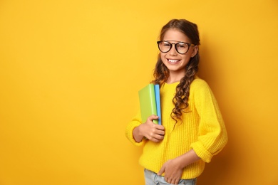 Image of Happy little girl with books on yellow background