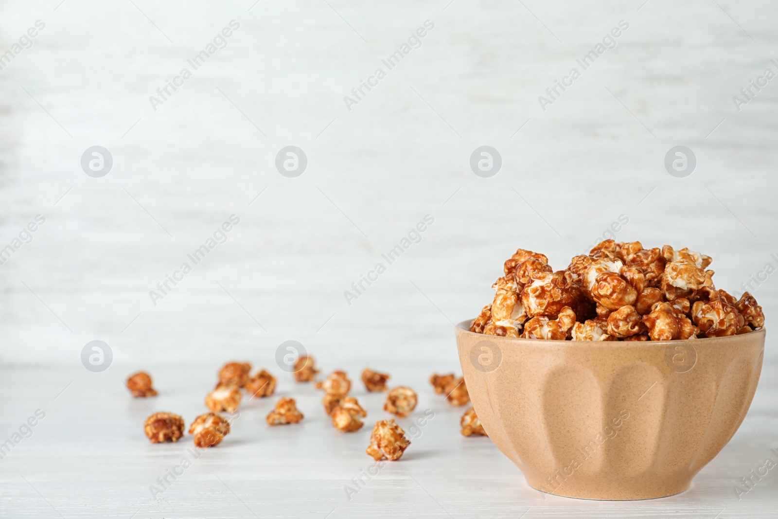 Photo of Bowl with tasty popcorn on white table. Space for text