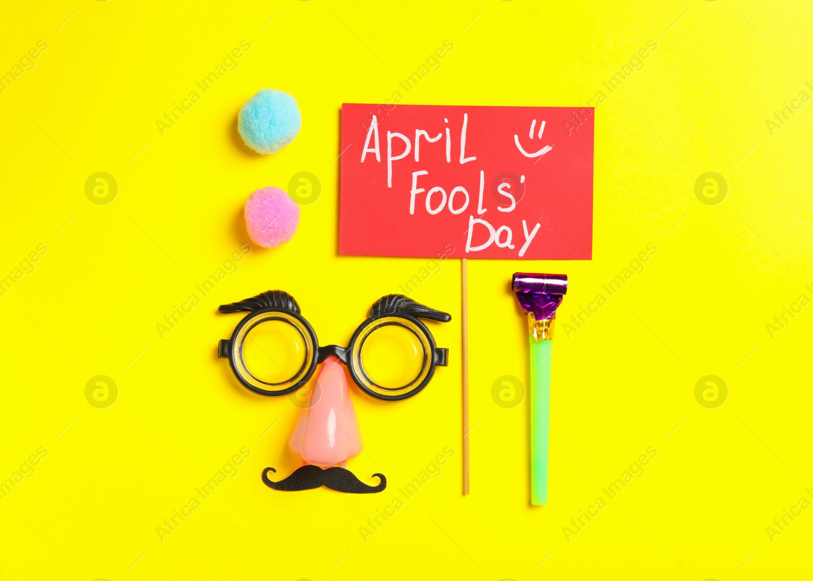 Photo of Sign with phrase April Fools' Day and different clown's accessories on yellow background, flat lay