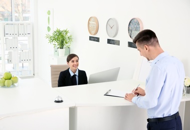 Young man filling form at reception desk in hotel