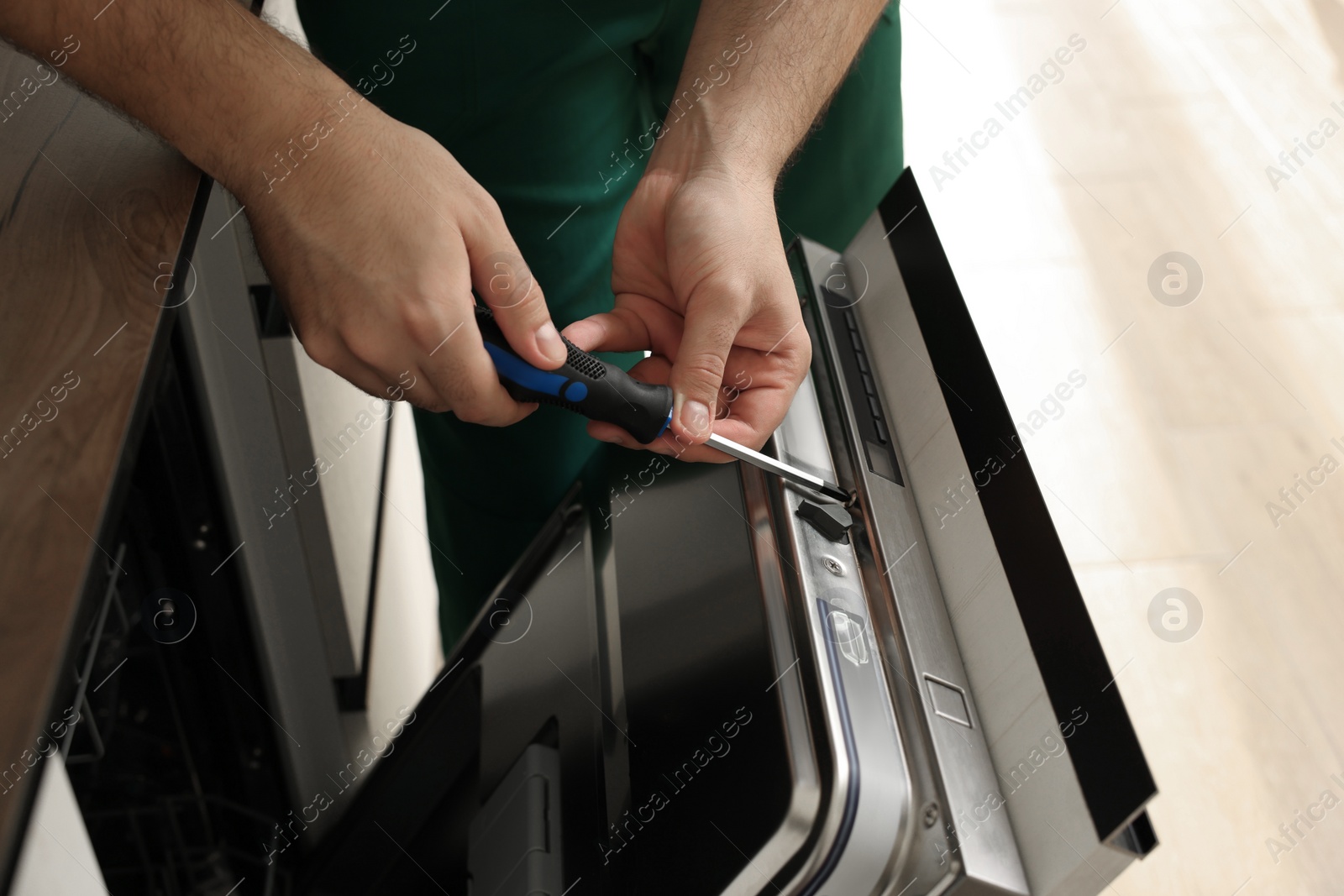 Photo of Serviceman repairing dishwasher door with screwdriver indoors, closeup