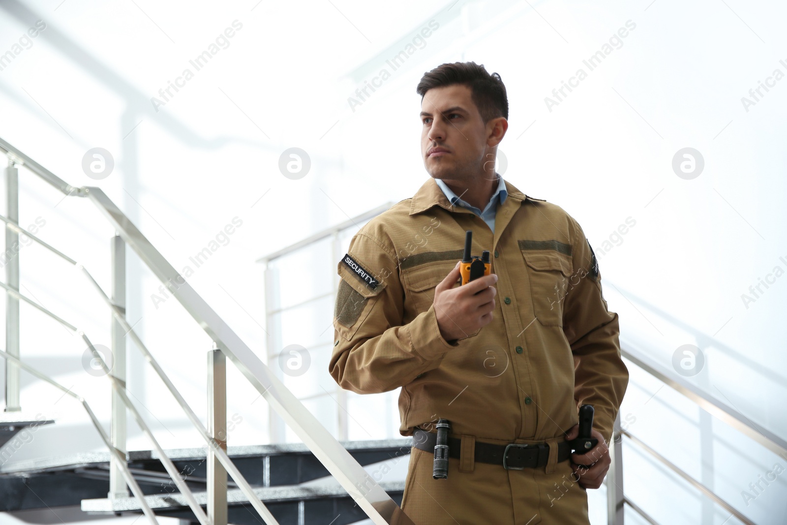 Photo of Professional security guard with portable radio set on stairs indoors