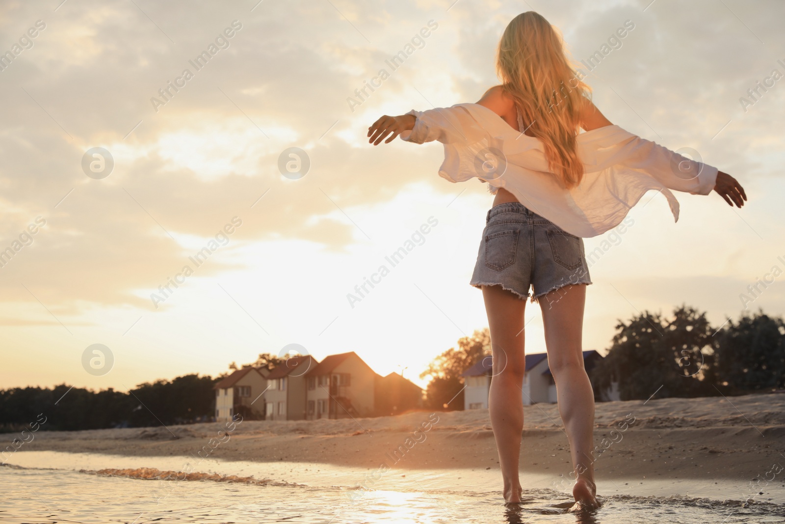 Photo of Beautiful young woman on beach at sunset, back view