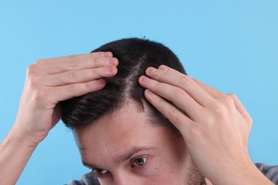 Photo of Man examining his hair and scalp on light blue background, closeup