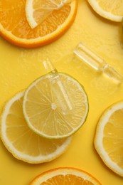 Photo of Skincare ampoules with vitamin C and citrus slices on yellow background, flat lay