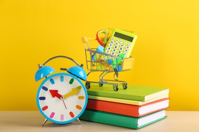 Photo of Different school stationery and alarm clock on table against yellow background. Back to school