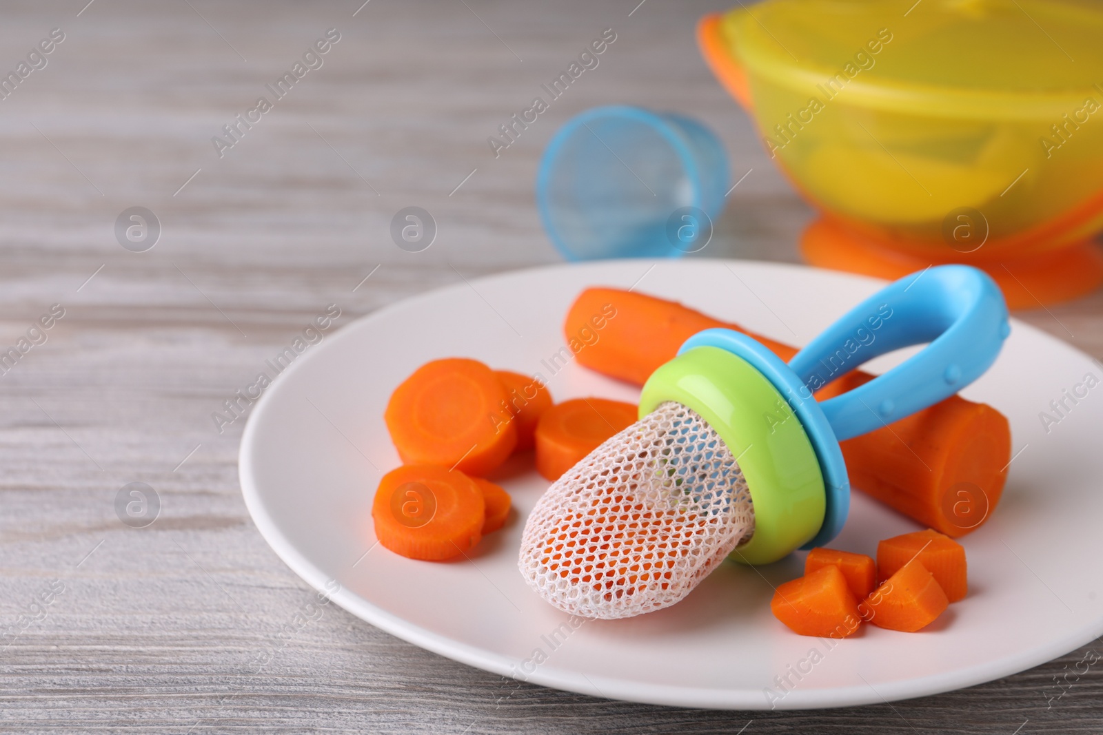 Photo of Nibbler with boiled carrot on white wooden table. Baby feeder