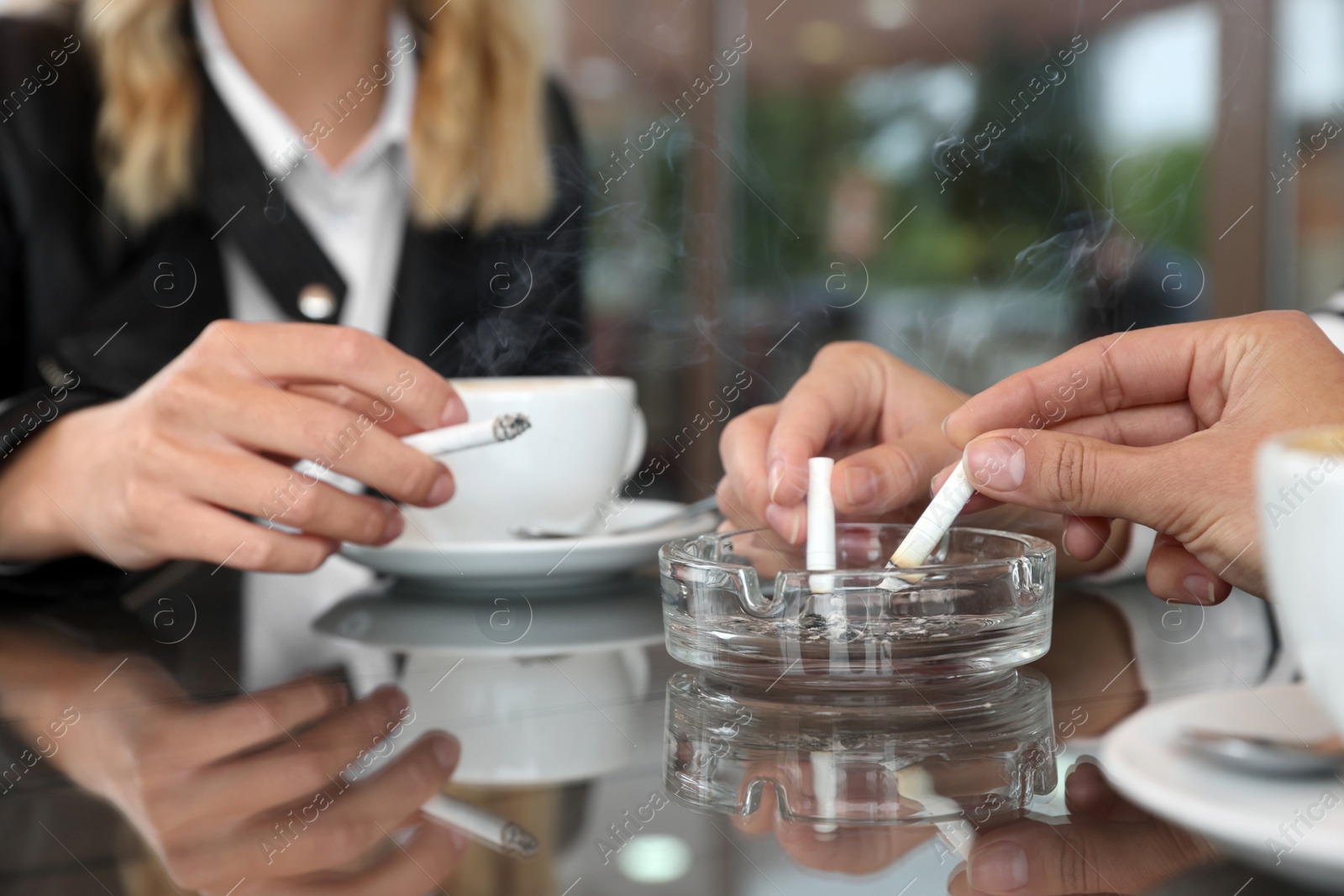 Photo of Women putting out cigarettes in ashtray at table, closeup