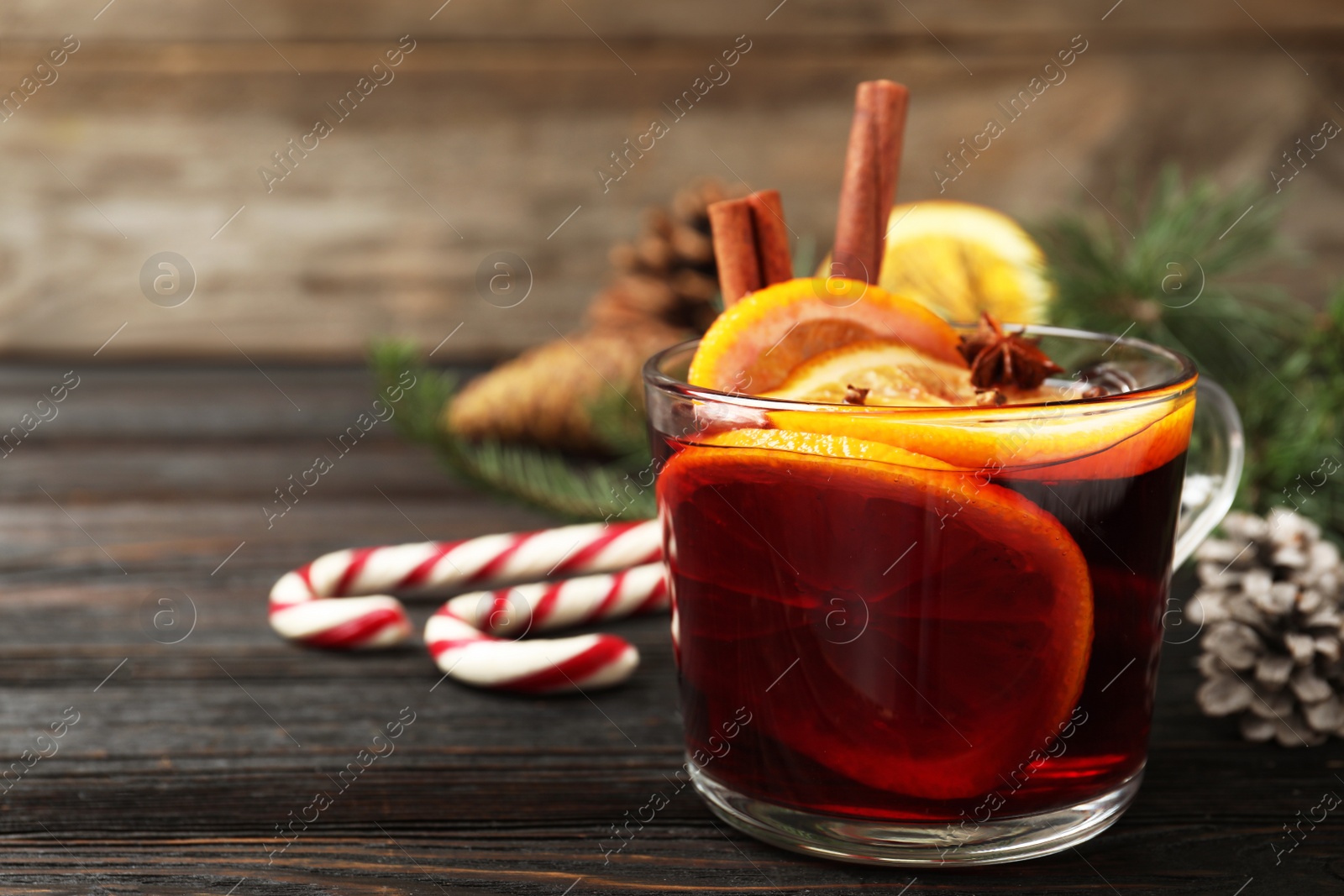 Photo of Glass cup of tasty mulled wine on black wooden table. Space for text