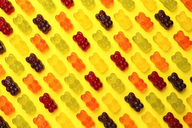 Photo of Delicious gummy bear candies on yellow background, flat lay