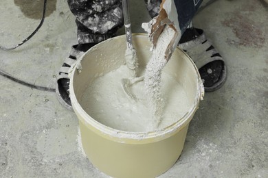 Photo of Professional worker mixing plaster in bucket indoors, closeup