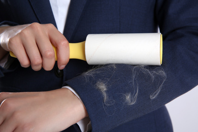 Photo of Woman removing cat hair from dark blue jacket with lint roller, closeup