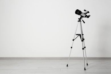 Photo of Tripod with modern telescope near white wall. Space for text
