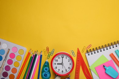 Photo of Flat lay composition with different school stationery and alarm clock on yellow background, space for text. Back to school