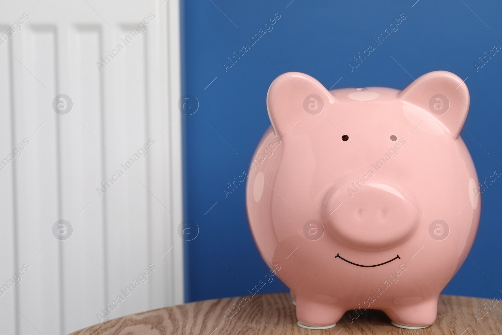 Photo of Piggy bank on wooden table near heating radiator, space for text