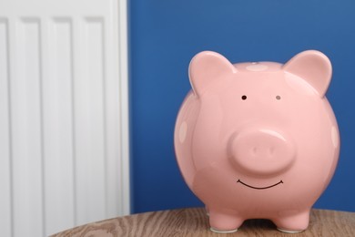 Piggy bank on wooden table near heating radiator, space for text