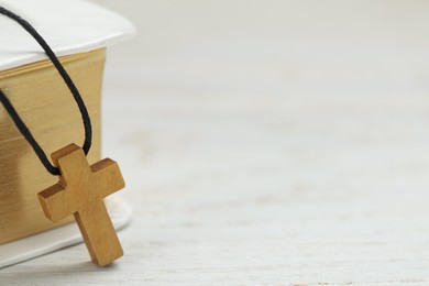 Photo of Wooden Christian cross and Bible on white table, closeup. space for text
