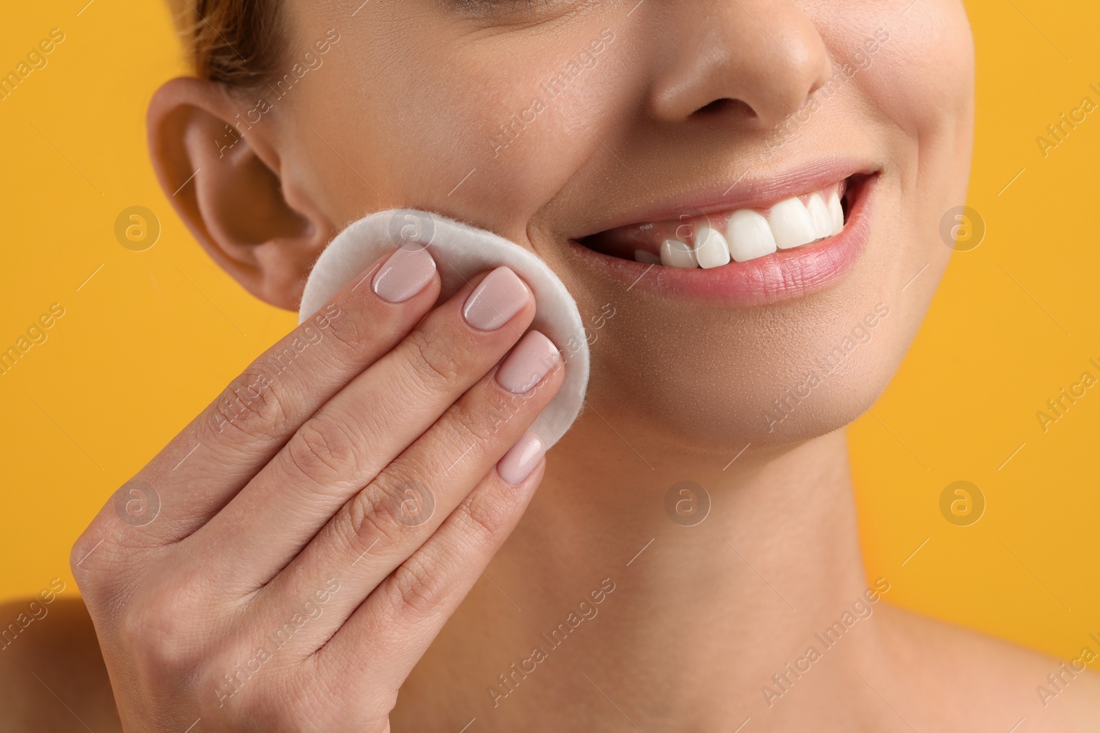 Photo of Smiling woman removing makeup with cotton pad on yellow background, closeup