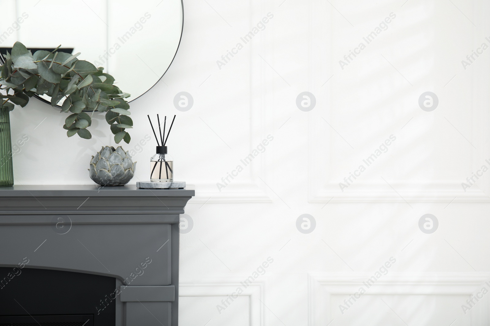 Photo of Reed diffuser and home decor on grey mantelpiece near white wall. Space for text