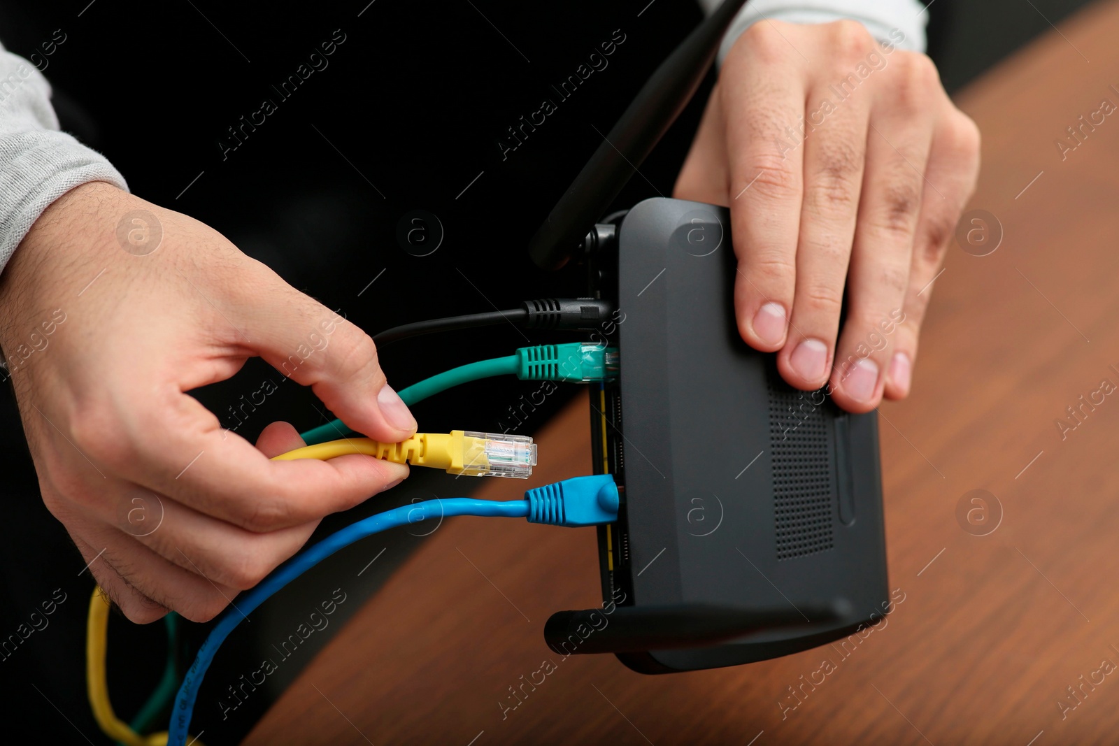 Photo of Man inserting cable into Wi-Fi router at wooden table indoors, closeup