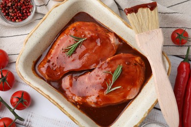 Flat lay composition with raw marinated meat in baking dish, products and basting brush on white wooden table