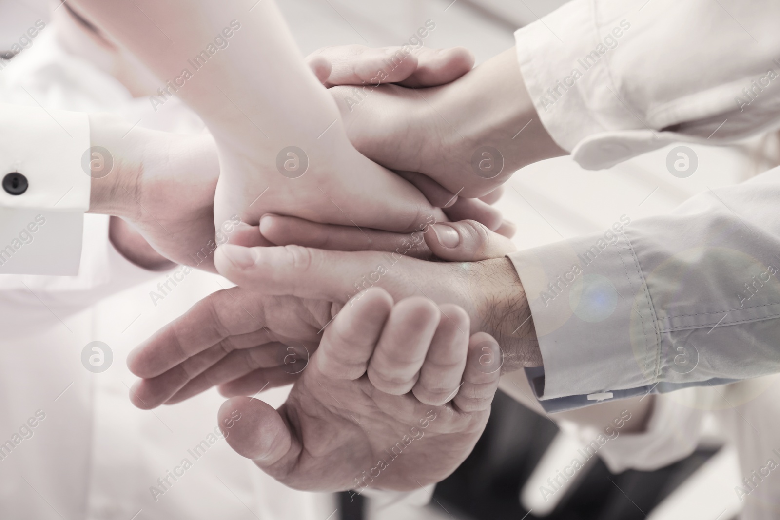 Image of People holding hands together in office, closeup. Black and white effect