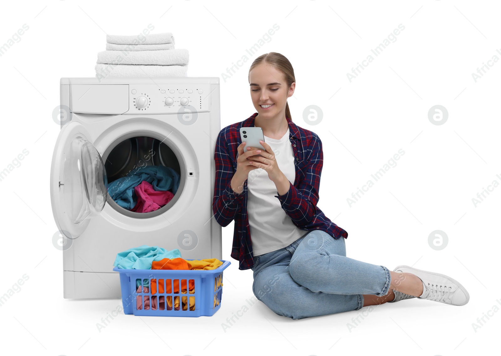 Photo of Beautiful young woman using smartphone near washing machine with laundry against white background