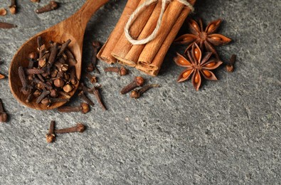 Photo of Wooden spoon with different spices on gray textured table, flat lay. Space for text